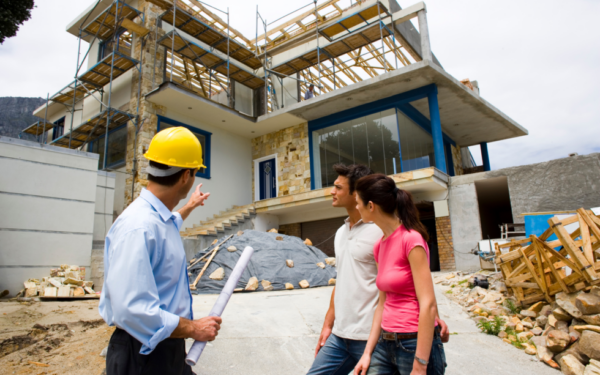 Roofer contractor points at home in progress of being built in front of a couple
