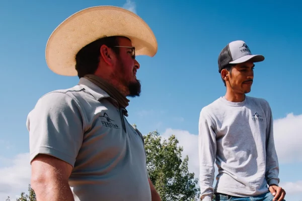 Two construction workers wearing light-colored clothes and hats to keep off the sun and stay cool while working outside in the summer