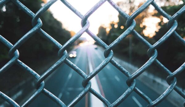 Close up of chainlink fence with road and trees in the background